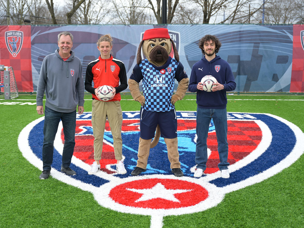 Representatives from the Indy Eleven and their mascot Zeke standing on the Indy Eleven logo in the museum's Soccer Experience.